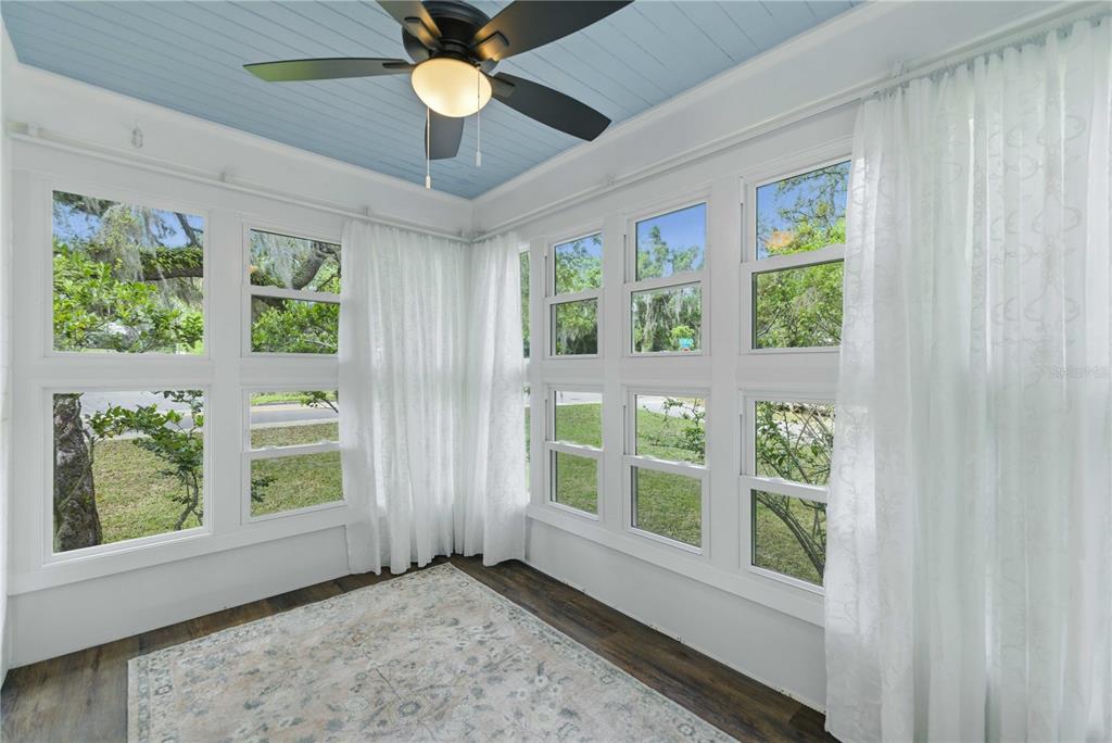 A sunroom features a blue ceiling, a ceiling fan, white curtains, and large windows — 923 NE 2ND STREET, OCALA, FL