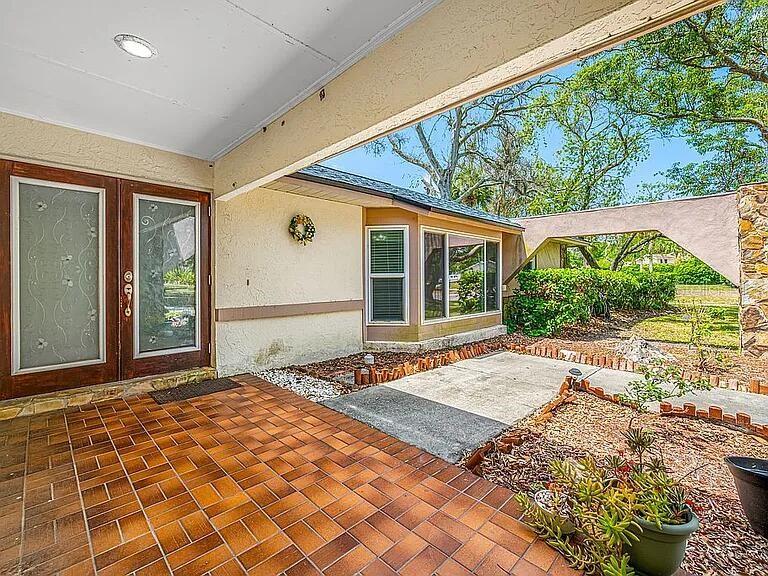 A covered patio with tiled flooring leads to a house entrance with glass-paneled double doors — 10 LINDEN LANE, PALM HARBOR, FL