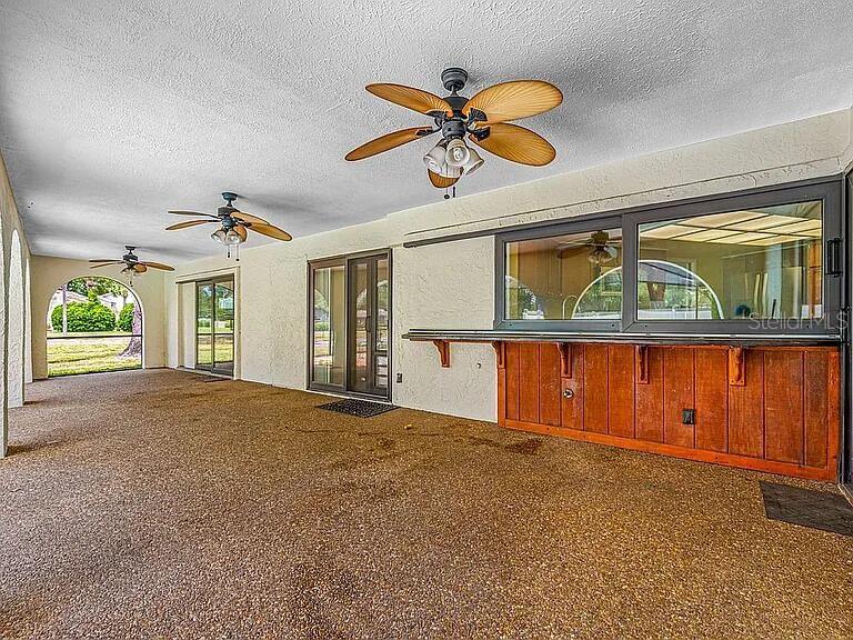 A covered patio features a textured floor, three ceiling fans, and a wooden bar counter — 10 LINDEN LANE, PALM HARBOR, FL