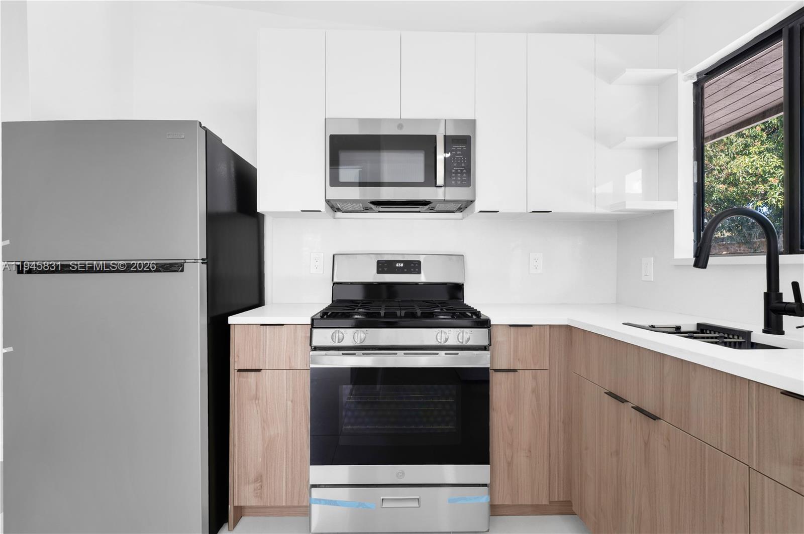 A modern kitchen features white upper cabinets, light wood lower cabinets, and stainless steel appliances — 3040 NW 93rd # D, Miami FL 33147, MIAMI, FL