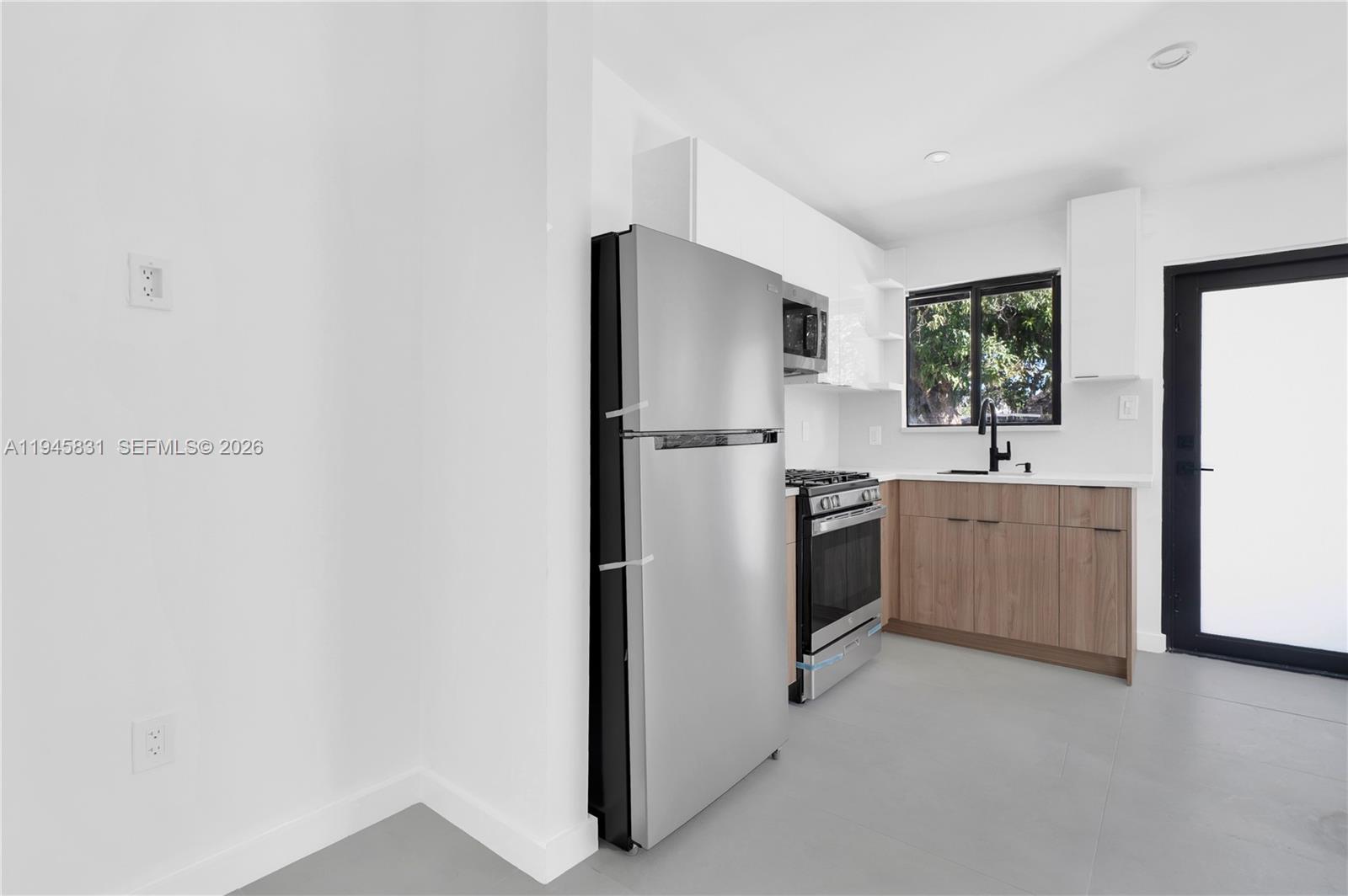 A modern kitchen features stainless steel appliances, wood-tone cabinets, and white walls — 3040 NW 93rd # D, Miami FL 33147, MIAMI, FL