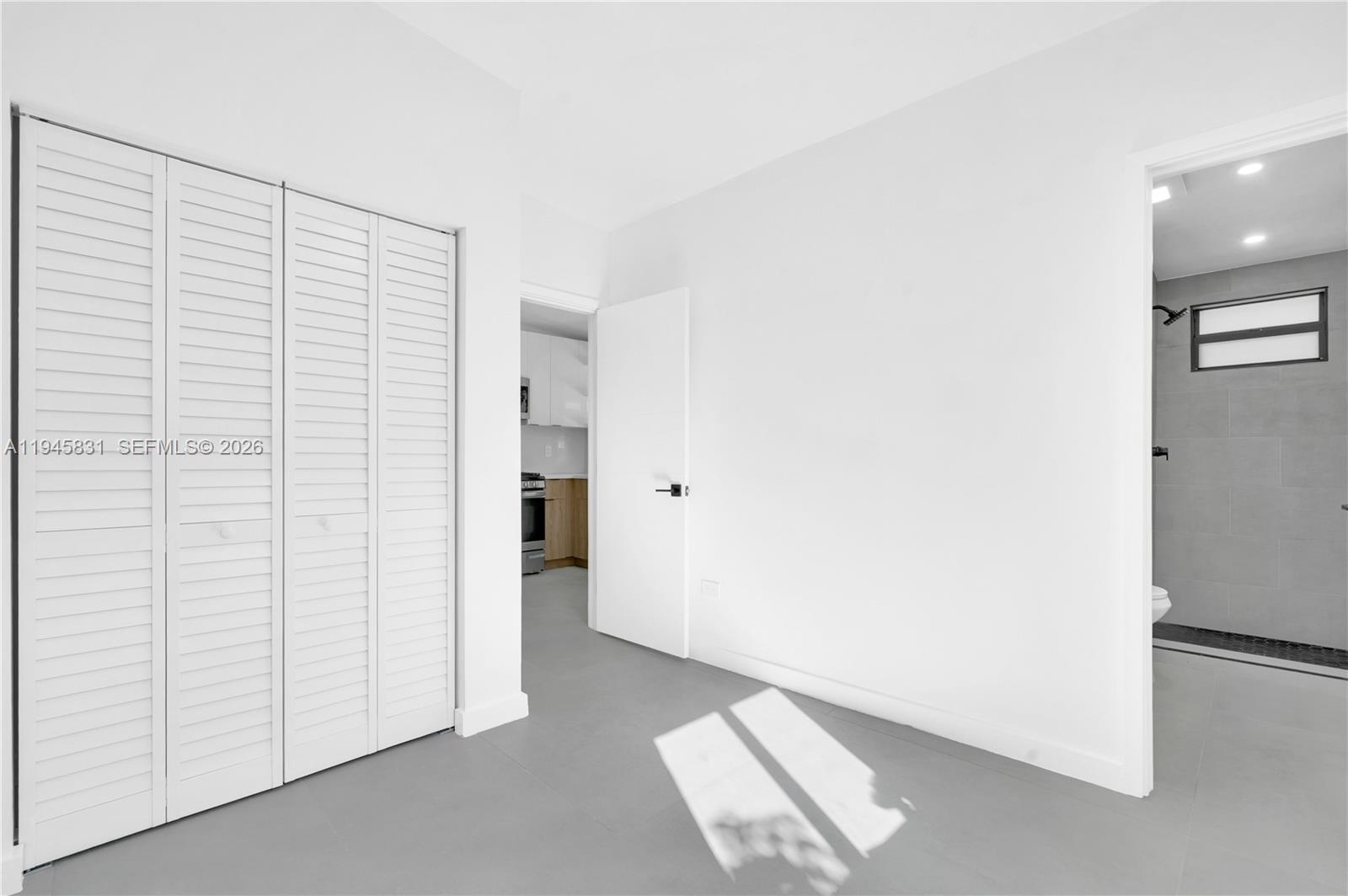 A room with white walls, gray tile flooring, a louvered closet, and an attached bathroom — 3040 NW 93rd # D, Miami FL 33147, MIAMI, FL