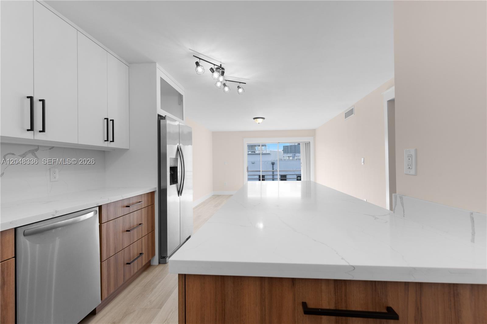 A modern kitchen features white upper cabinets, wood-tone lower cabinets, and a large quartz island — 8752 SW 12th St # 201, Miami FL 33174, MIAMI, FL