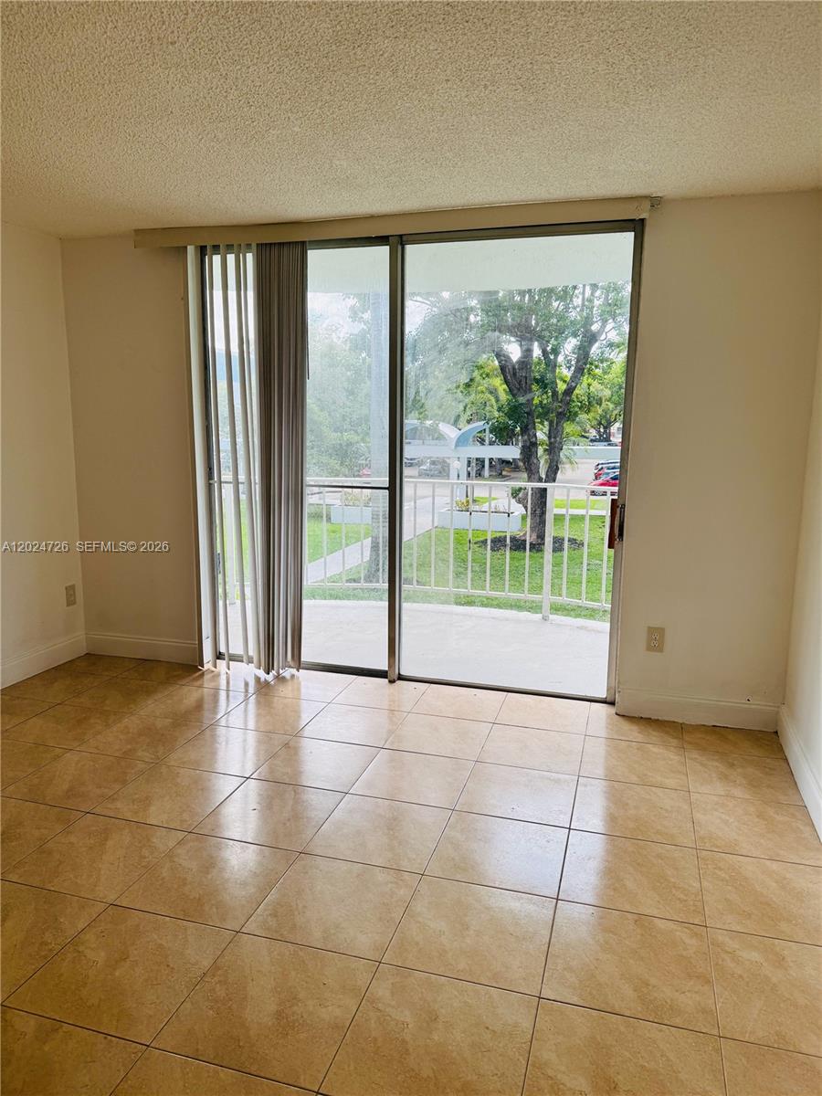 A room with beige tile flooring features a sliding glass door leading to a balcony — 486 NW 165th St Rd # 201, Miami FL 33169, MIAMI, FL