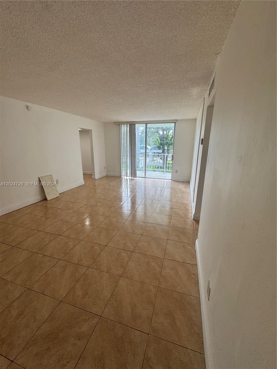An empty living room features beige tile flooring, white walls, and a sliding glass balcony door — 486 NW 165th St Rd # 201, Miami FL 33169, MIAMI, FL