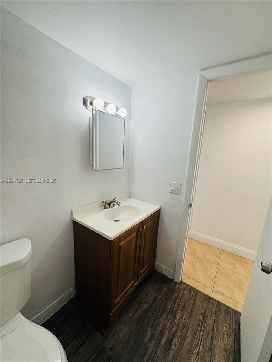 A bathroom features a wooden vanity, a white sink, a medicine cabinet, and dark flooring — 486 NW 165th St Rd # 201, Miami FL 33169, MIAMI, FL