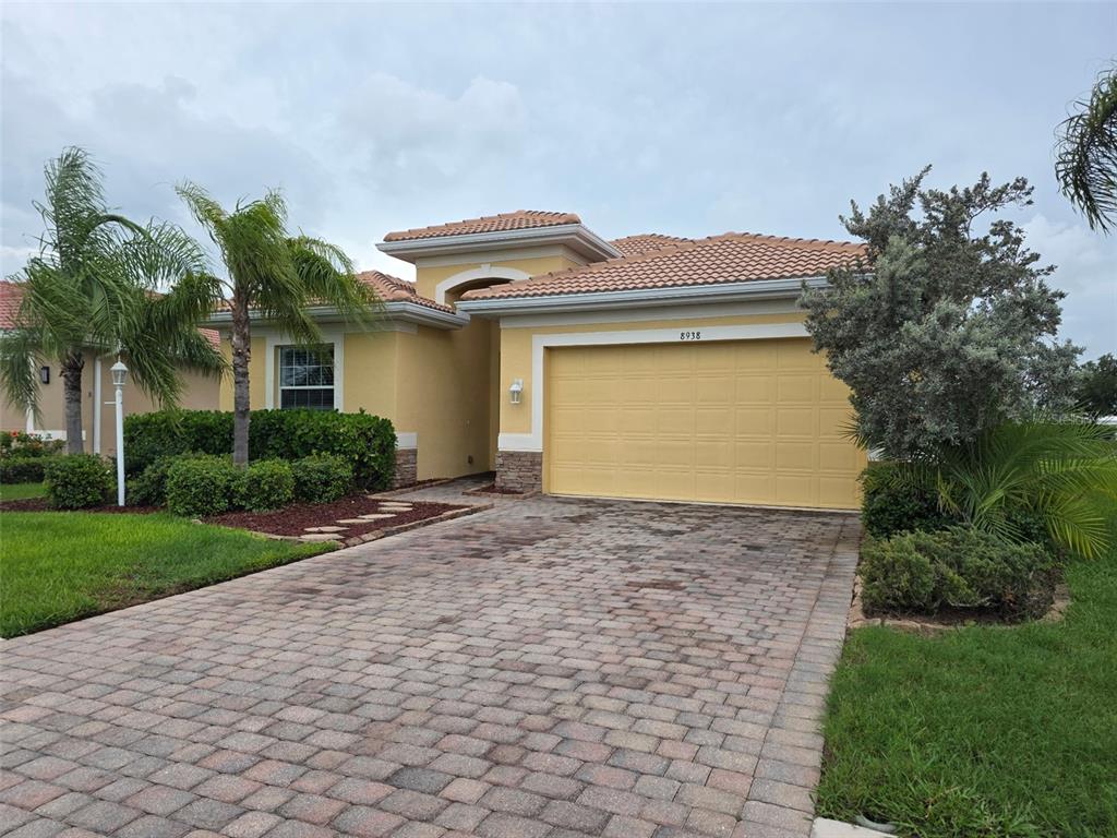 A single-story yellow house features a two-car garage, a paved driveway, and palm trees — 8938 PEREGRINE WAY, NORTH PORT, FL