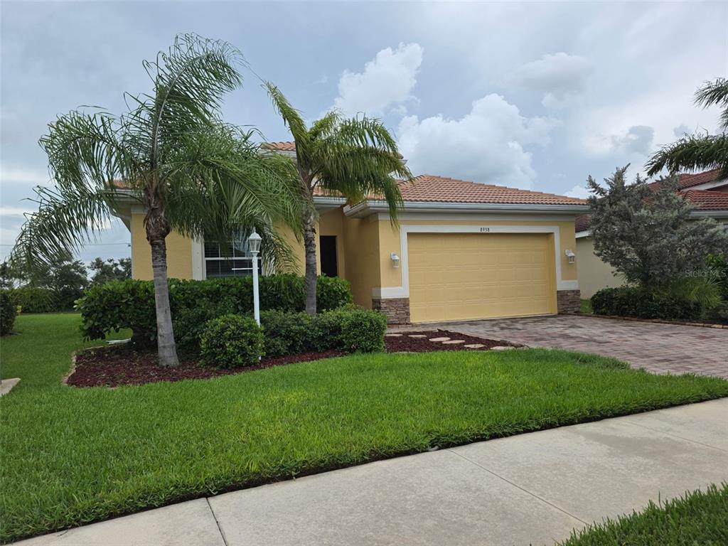 A yellow house exterior features a palm tree, a stone-accented garage, and a paved walkway — 8938 PEREGRINE WAY, NORTH PORT, FL