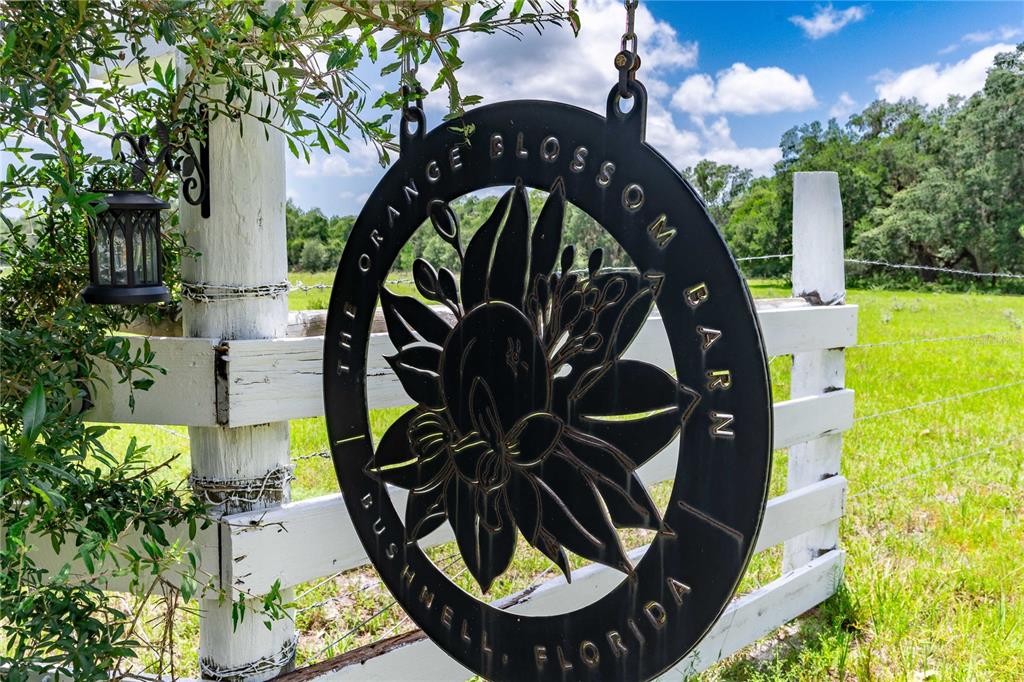 A round metal sign for The Orange Blossom Barn hangs on a white fence — 4773 SW 47TH BOULEVARD, BUSHNELL, FL