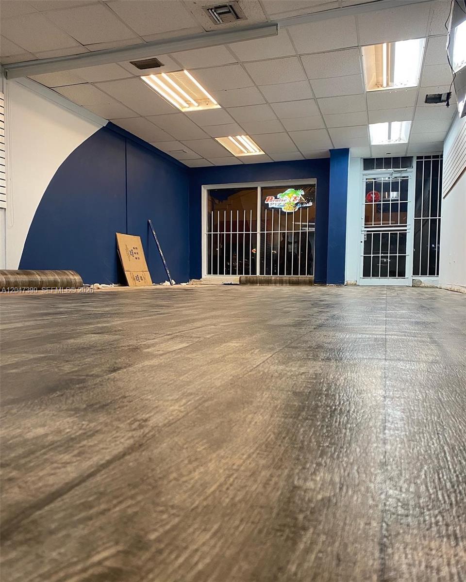 An empty commercial space features dark blue walls, wood-look flooring, and a security-barred storefront entrance — 450 Palm Ave, Hialeah FL 33010, HIALEAH, FL