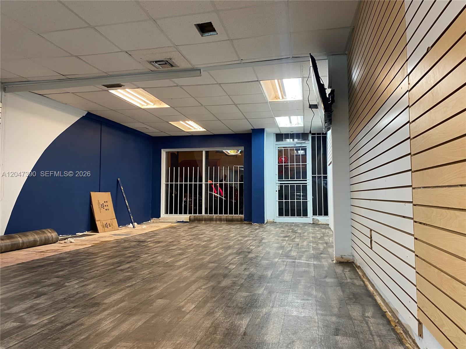 An empty commercial space features wood-look flooring, a blue accent wall, and slat wall panels — 450 Palm Ave, Hialeah FL 33010, HIALEAH, FL