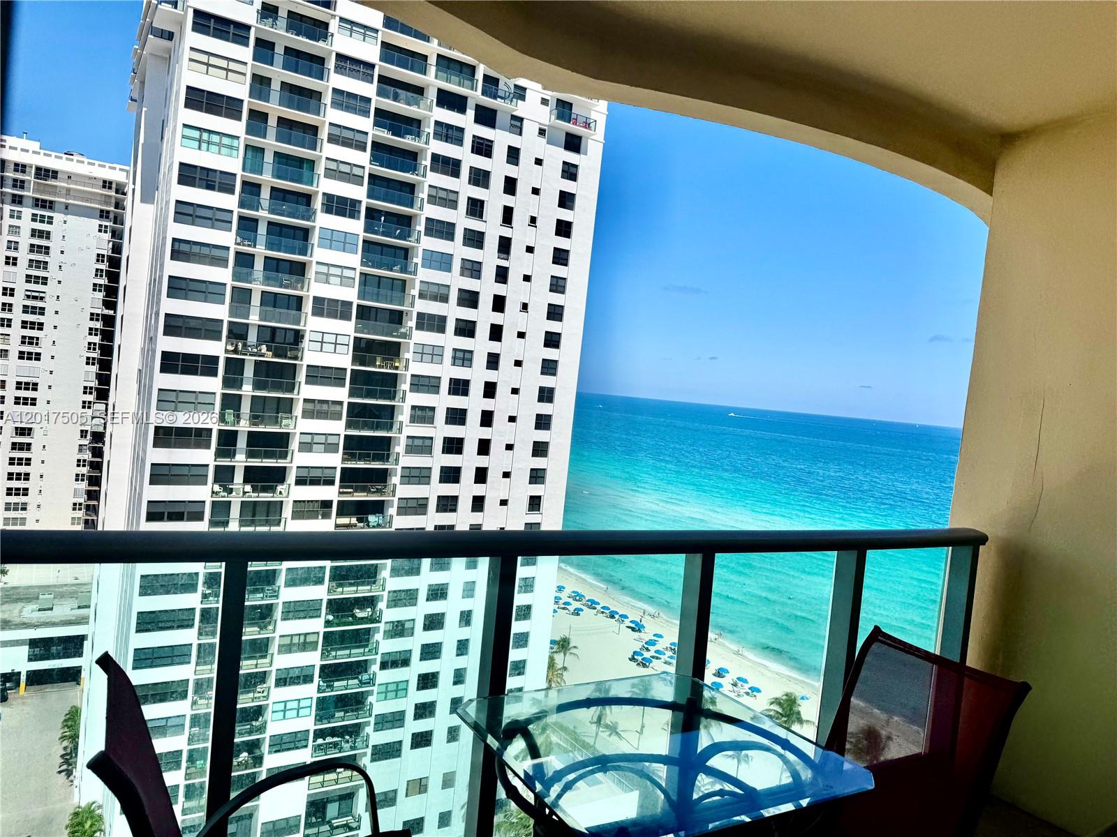 A balcony view features a glass table, two chairs, a neighboring high-rise, and the ocean — 2501 S Ocean Dr, Hollywood FL 33019, HOLLYWOOD, FL