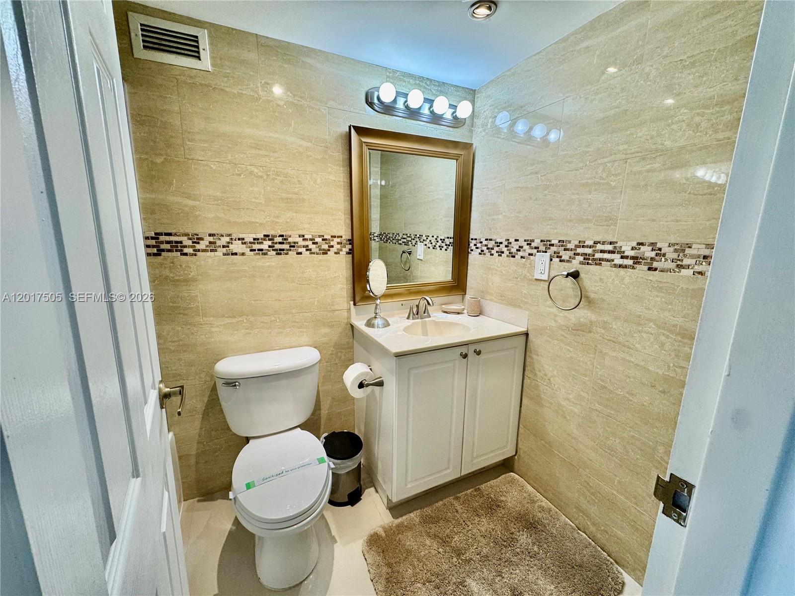 A small bathroom features beige tiled walls, a white vanity, and a toilet — 2501 S Ocean Dr, Hollywood FL 33019, HOLLYWOOD, FL
