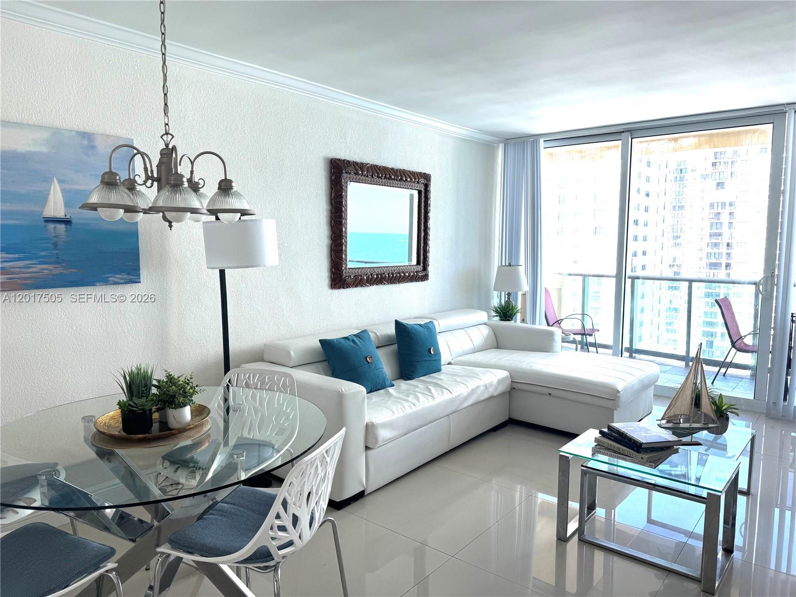 A bright living and dining area features a white sectional sofa, glass tables, and balcony access — 2501 S Ocean Dr, Hollywood FL 33019, HOLLYWOOD, FL