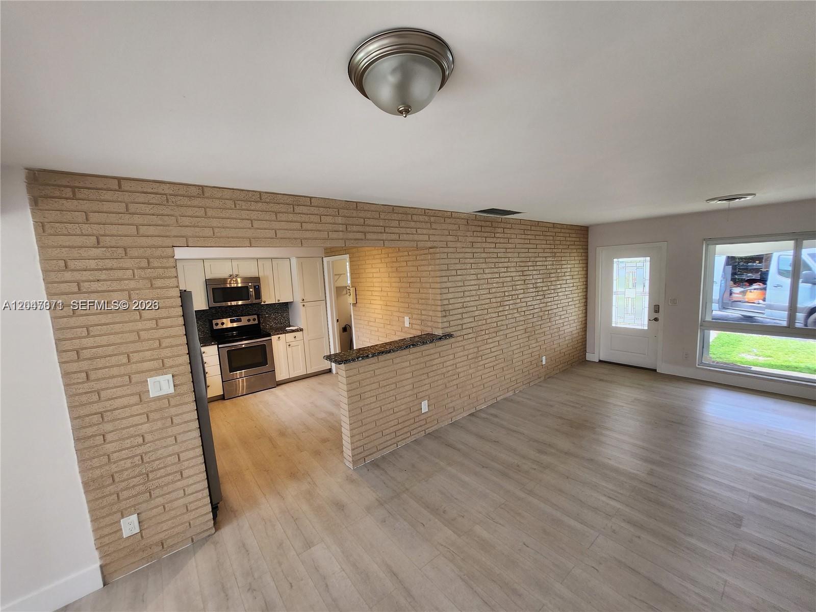 A kitchen with stainless steel appliances opens to a living area featuring a brick wall — 3346 Coolidge St, Hollywood FL 33021, HOLLYWOOD, FL