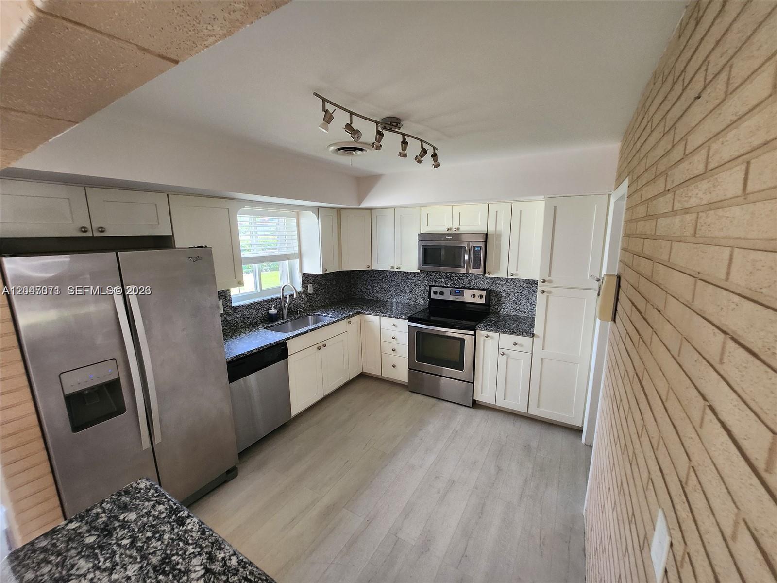 A kitchen features white cabinets, stainless steel appliances, granite countertops, and a brick wall — 3346 Coolidge St, Hollywood FL 33021, HOLLYWOOD, FL