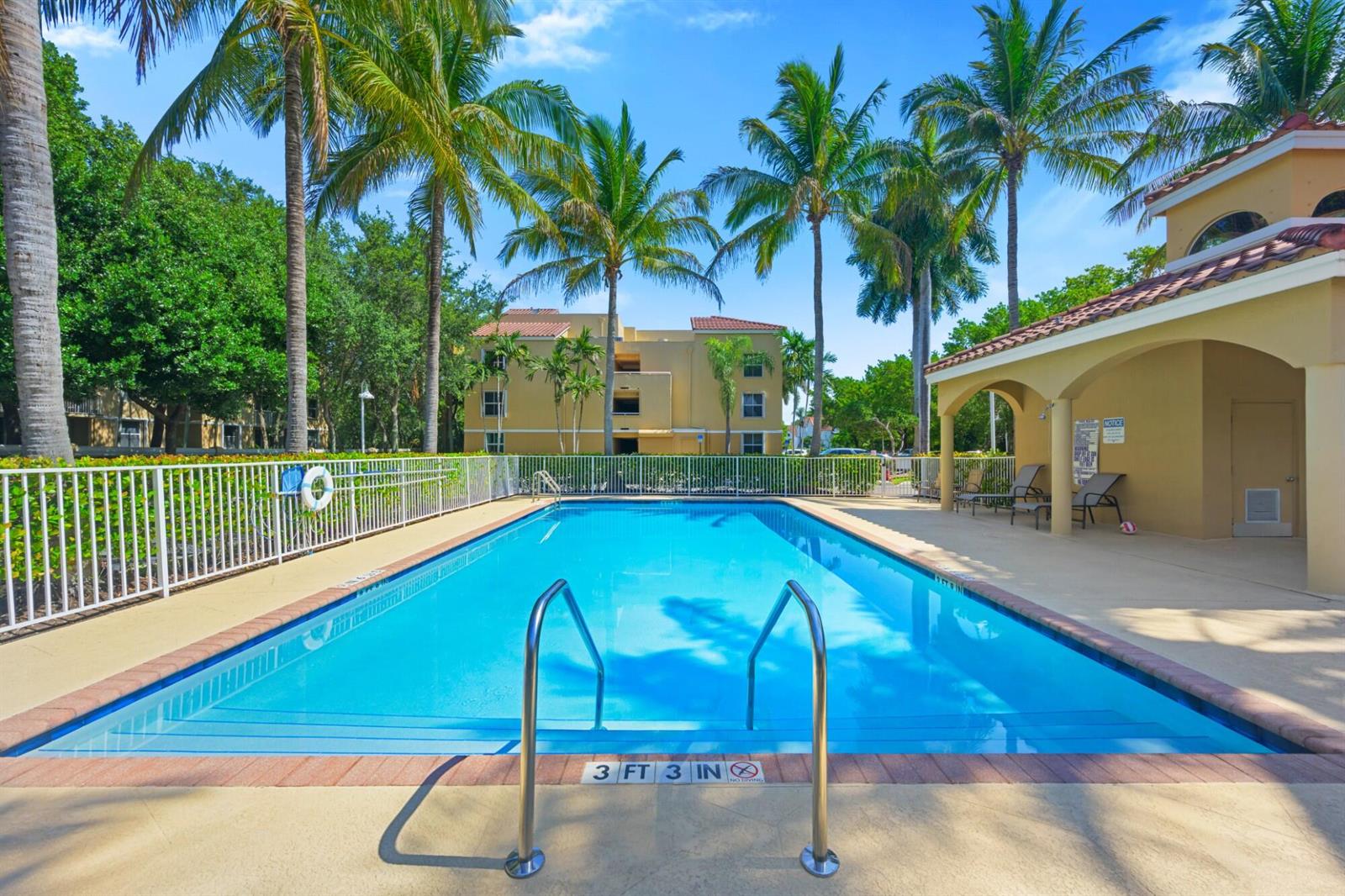 A rectangular swimming pool sits in front of a multi-story apartment building with palm trees — 619 E Sheridan Street # 106, Dania Beach FL 33004, DANIA BEACH, FL