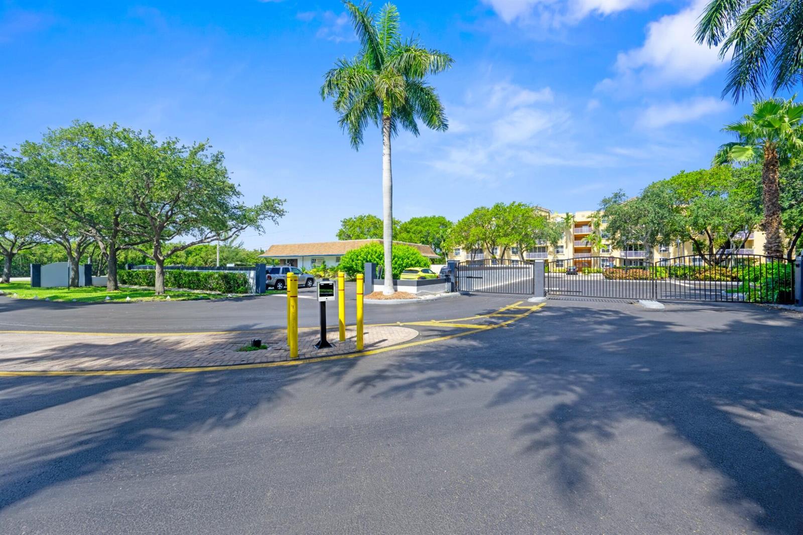 A gated entrance with a palm tree, yellow bollards, and a multi-story apartment building — 619 E Sheridan Street # 106, Dania Beach FL 33004, DANIA BEACH, FL
