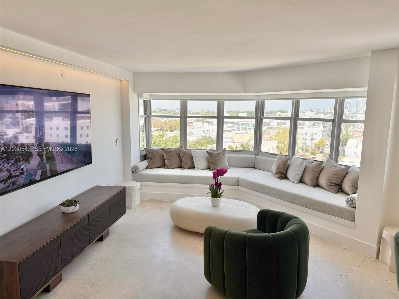 A modern living room features a built-in window bench, a dark green armchair, and television — 1881 Washington Ave # 9C, Miami Beach FL 33139, MIAMI BEACH, FL