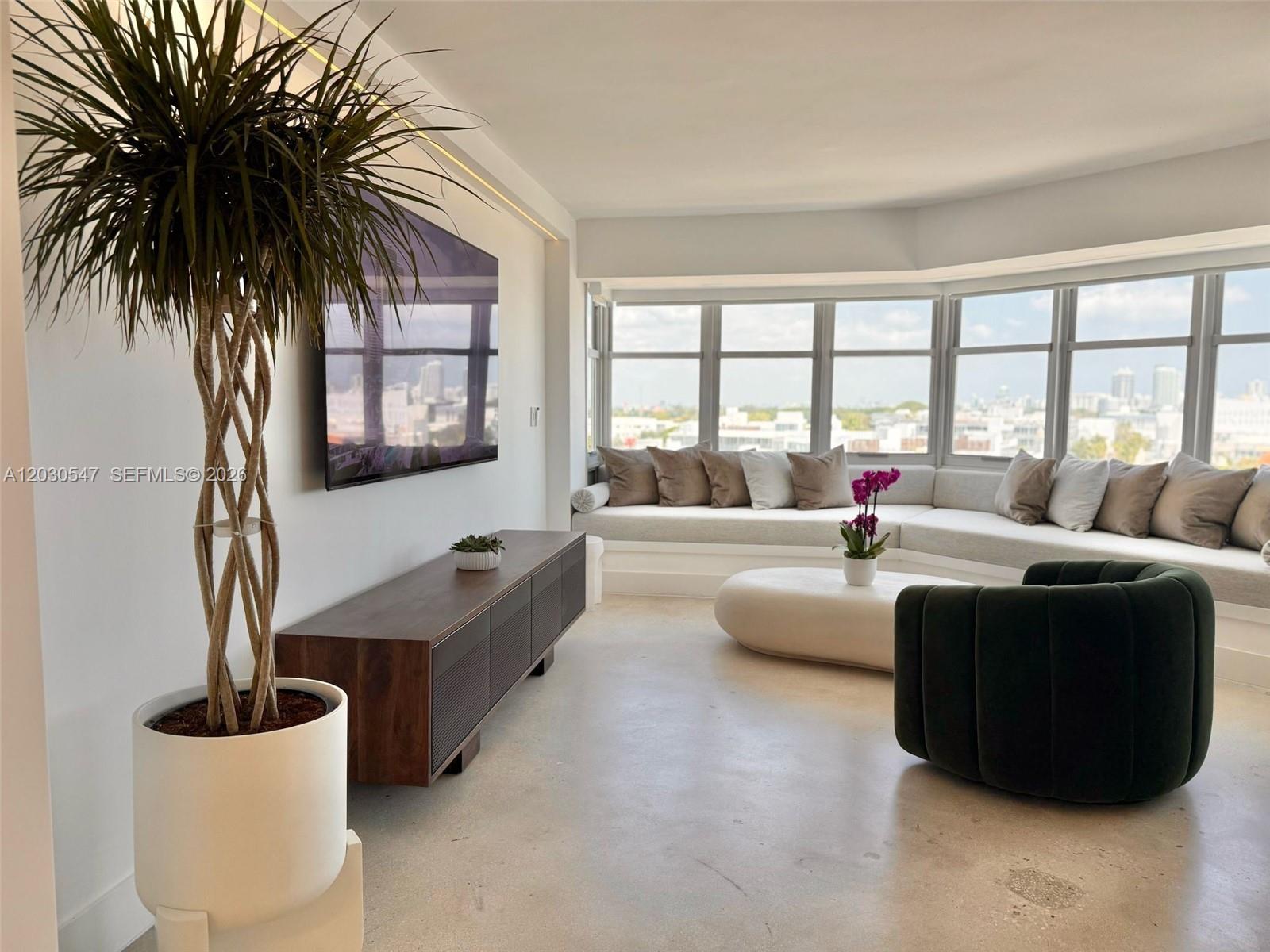 A modern living room features a large window, a built-in sofa, and a television — 1881 Washington Ave # 9C, Miami Beach FL 33139, MIAMI BEACH, FL