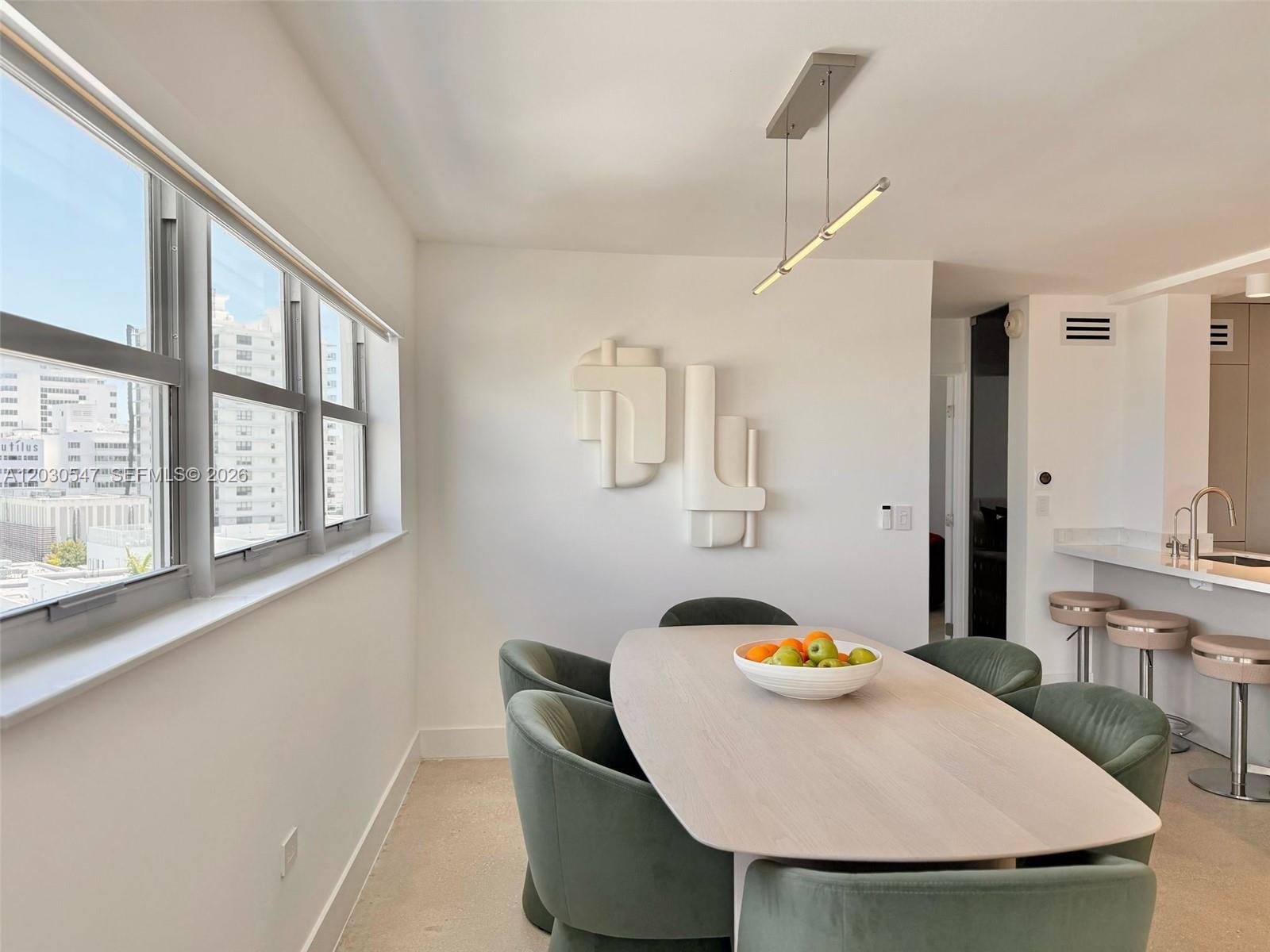 A dining area features a light wood table, green velvet chairs, and modern wall art — 1881 Washington Ave # 9C, Miami Beach FL 33139, MIAMI BEACH, FL