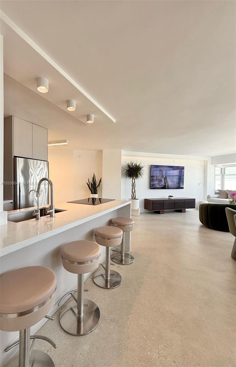 A modern kitchen with a breakfast bar and stools opens into a bright living area — 1881 Washington Ave # 9C, Miami Beach FL 33139, MIAMI BEACH, FL