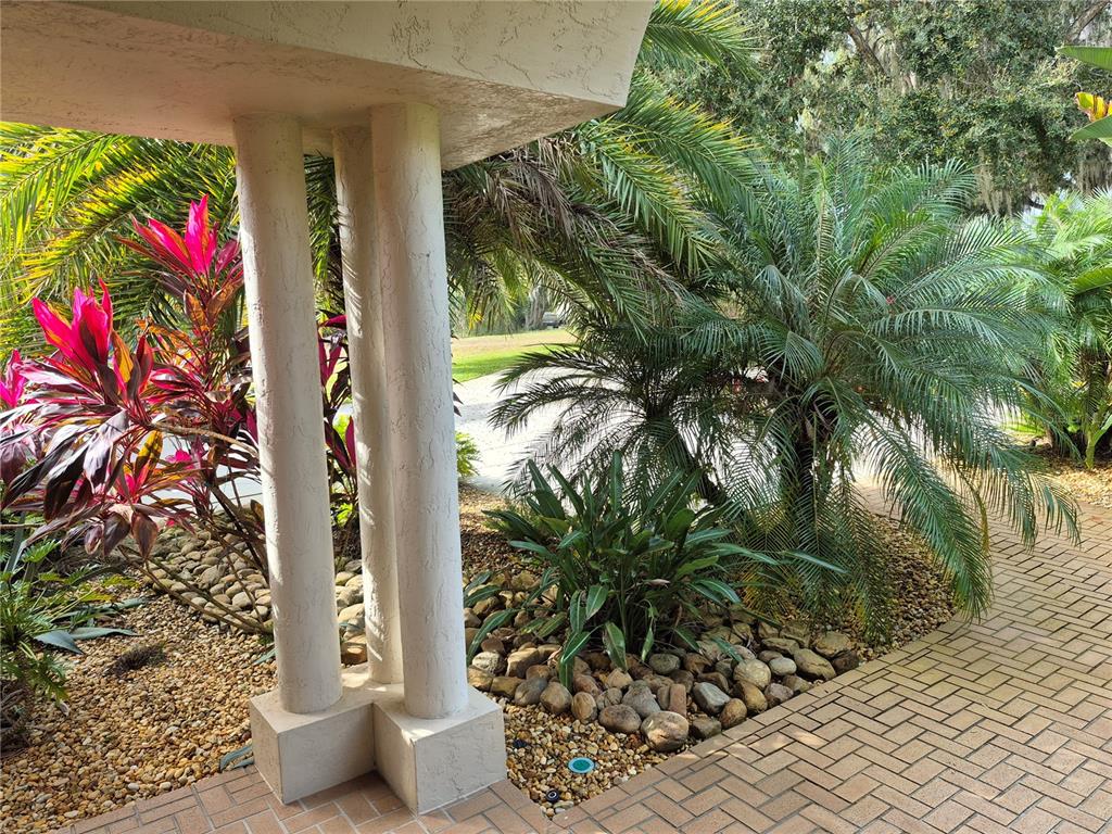 A paved walkway leads past a stucco pillar and tropical landscaping toward a driveway — 4345 CORLEY ISLAND ROAD, LEESBURG, FL