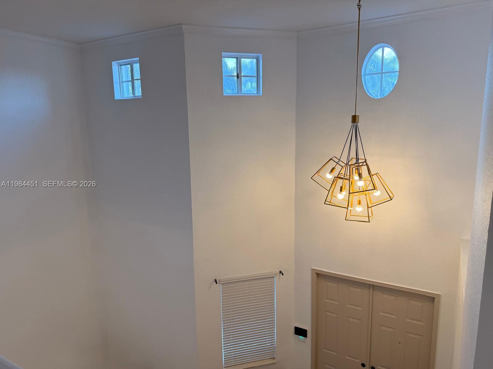 A high-ceilinged entryway features a geometric gold chandelier, three upper windows, and double doors — 16364 SW 63rd Ter, Miami FL 33193, MIAMI, FL