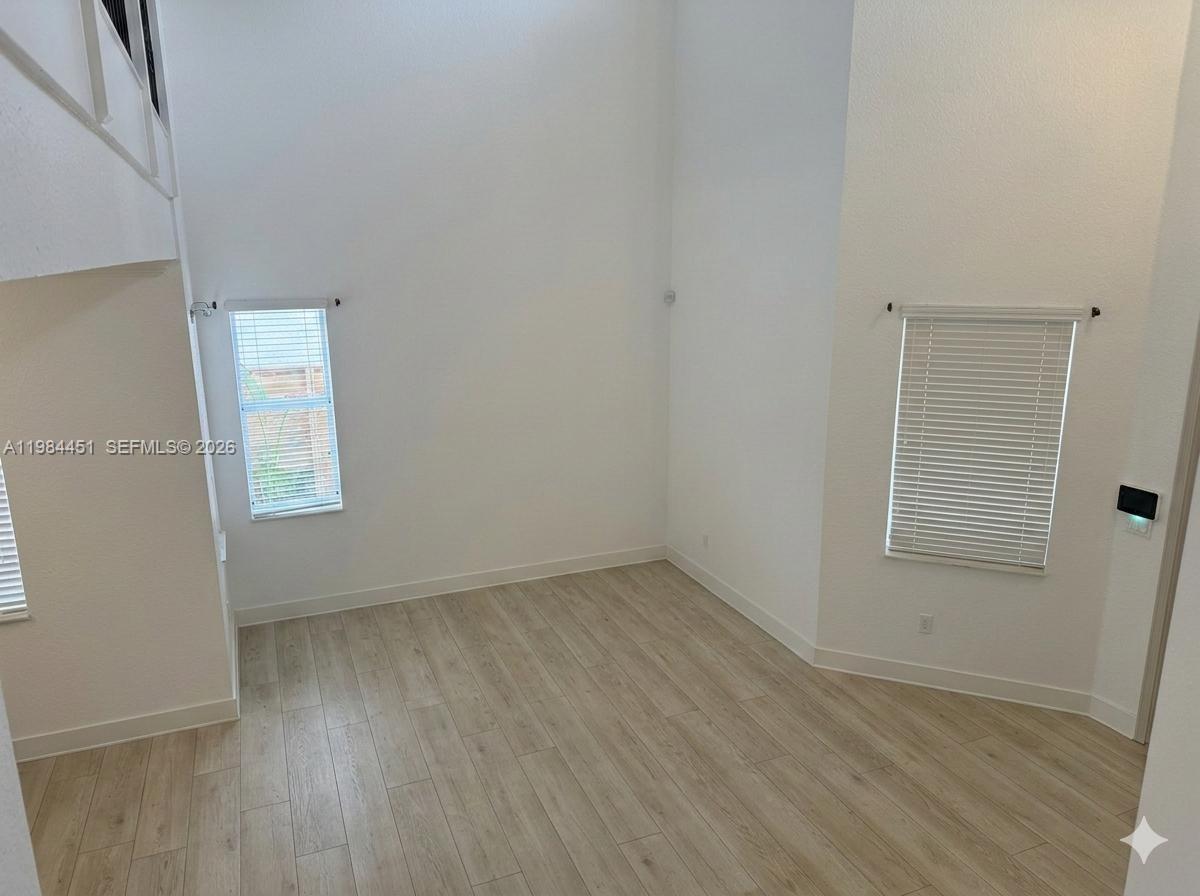 A bright room with high ceilings, light wood-look flooring, and two windows with blinds — 16364 SW 63rd Ter, Miami FL 33193, MIAMI, FL