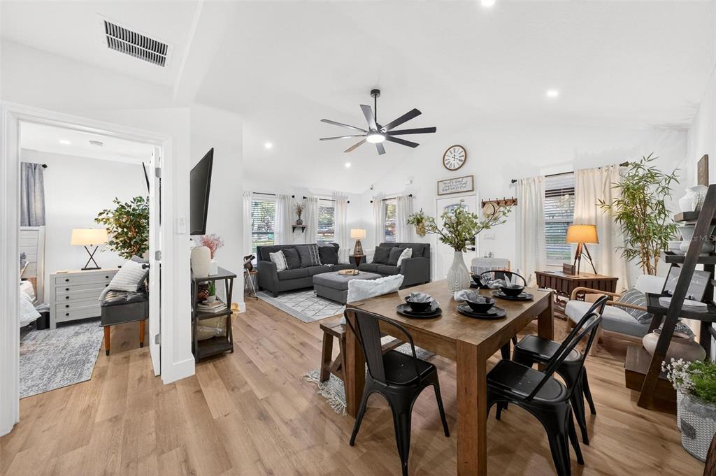 An open-concept living and dining area features wood-look flooring, a ceiling fan, and white walls — 1503 GRANITE STATE COURT, MOUNT DORA, FL