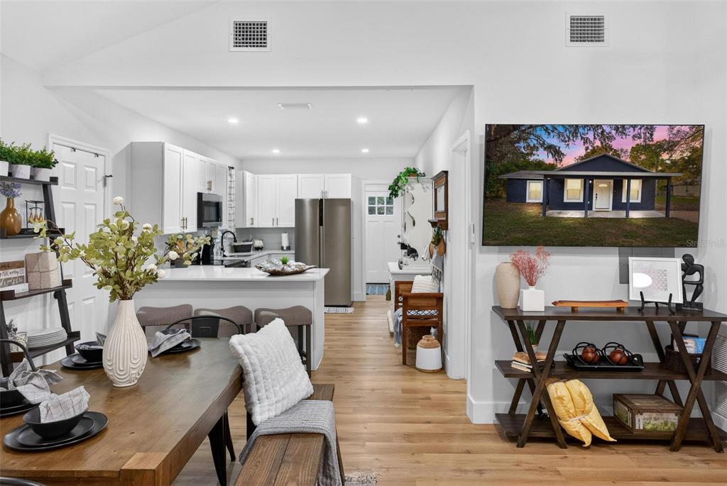 A dining area opens into a white kitchen with stainless steel appliances and wood flooring — 1503 GRANITE STATE COURT, MOUNT DORA, FL