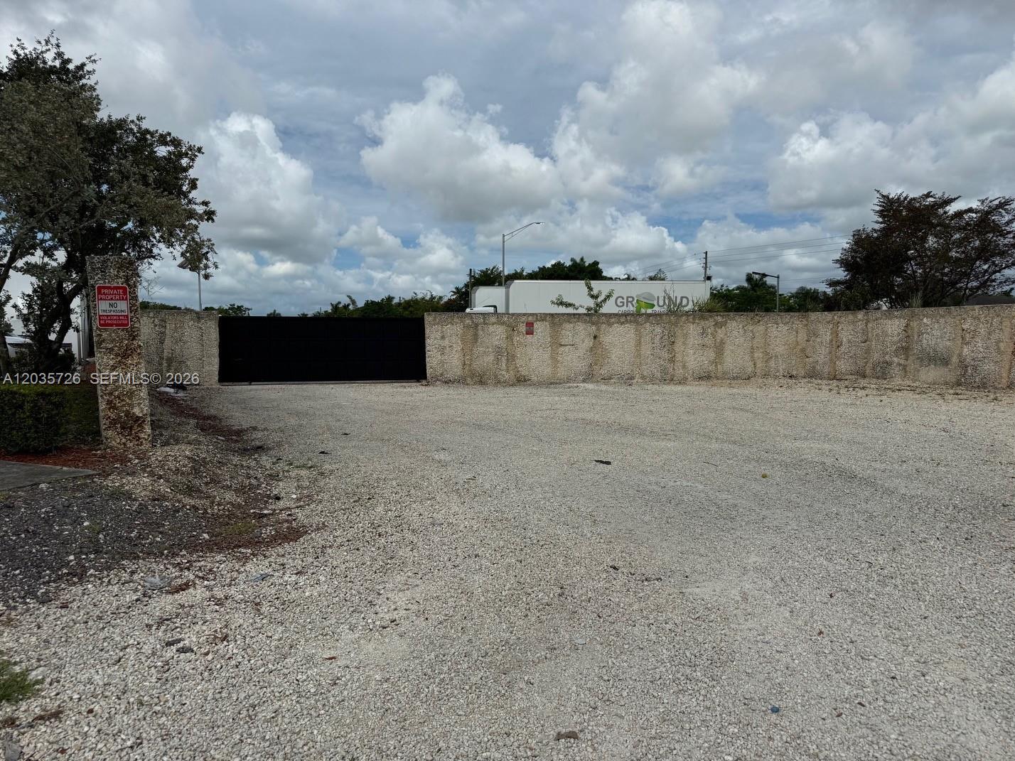 A gravel lot leads to a black gate in a stone wall with a trailer — SW 157th, Homestead FL 33033, HOMESTEAD, FL