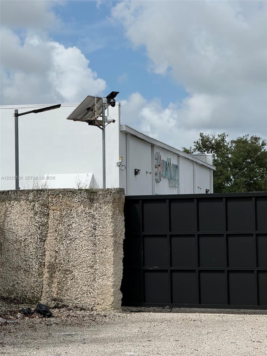 A black metal gate stands before a white building with a solar-powered security camera — SW 157th, Homestead FL 33033, HOMESTEAD, FL