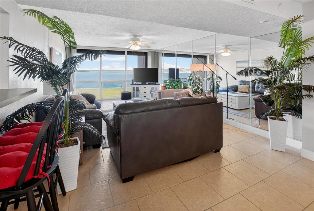 A living room features tiled floors, a mirrored wall, and a view of the water — 1 KEY CAPRI UNIT 103E, TREASURE ISLAND, FL
