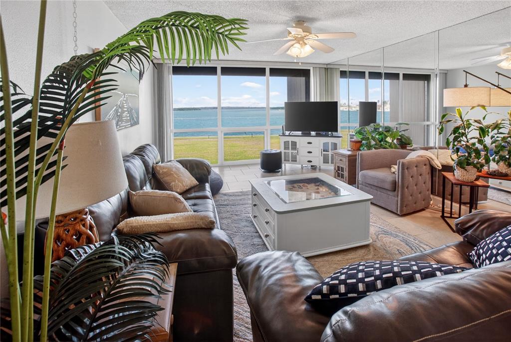 A living room features leather sofas, a coffee table, and large windows overlooking the water — 1 KEY CAPRI UNIT 103E, TREASURE ISLAND, FL