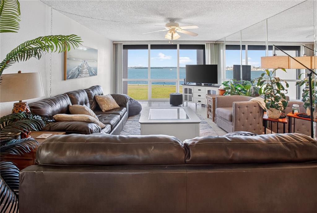 A living room features two leather sofas, a coffee table, and floor-to-ceiling waterfront windows — 1 KEY CAPRI UNIT 103E, TREASURE ISLAND, FL