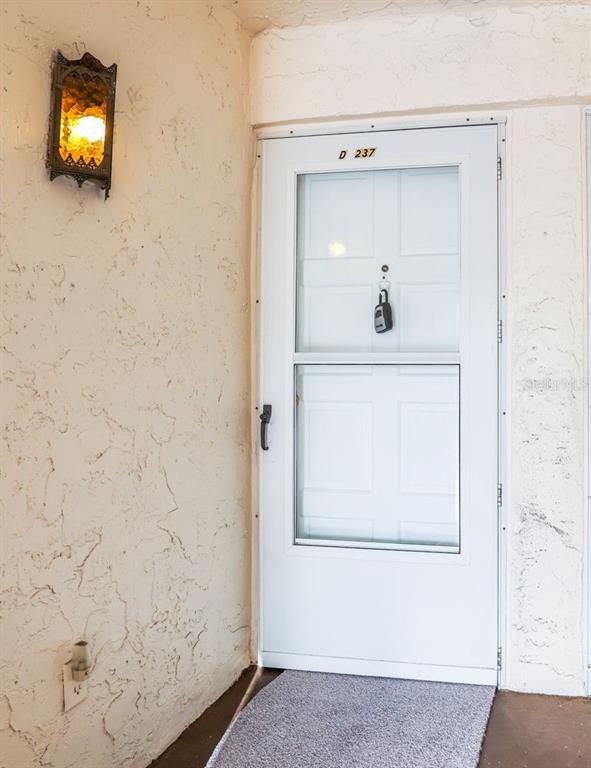 A white storm door with a lockbox hangs on a textured exterior wall — 225 COUNTRY CLUB DRIVE UNIT D237, LARGO, FL
