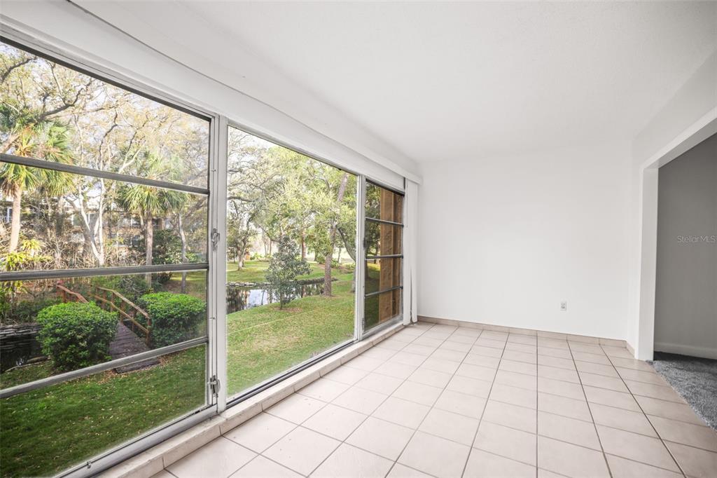 A sunroom with white walls, tiled flooring, and large windows overlooking a grassy outdoor area — 225 COUNTRY CLUB DRIVE UNIT D237, LARGO, FL