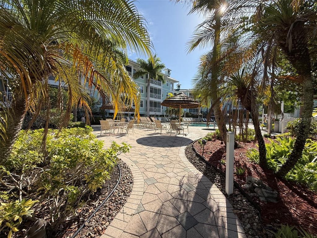 A paved walkway leads through a landscaped courtyard toward a swimming pool and apartment building — 5119 MELBOURNE STREET UNIT C304, PUNTA GORDA, FL