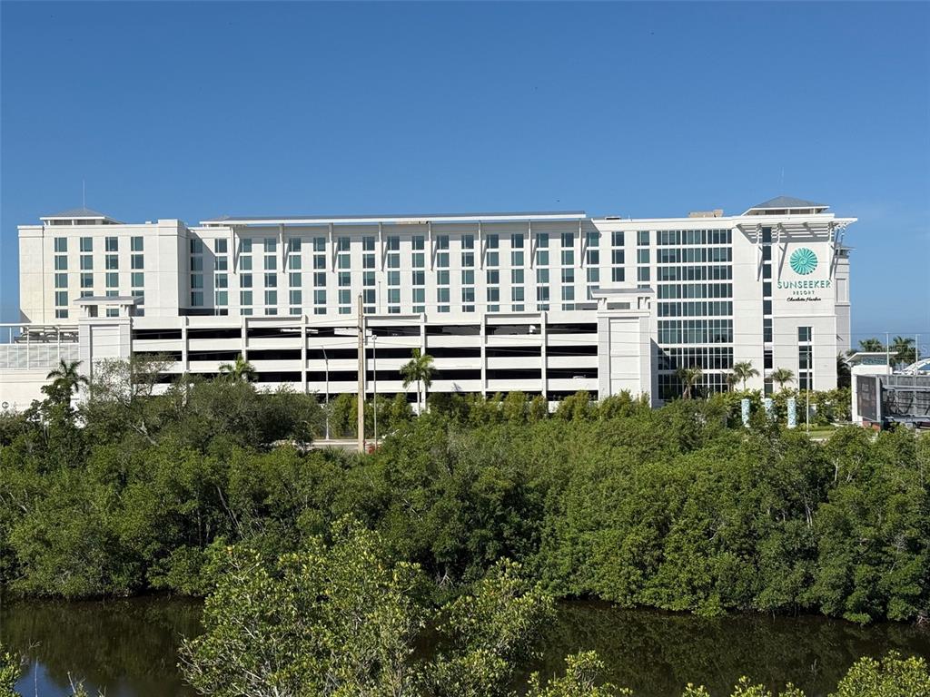 A large, multi-story white resort building stands behind a dense line of green trees — 5119 MELBOURNE STREET UNIT C304, PUNTA GORDA, FL