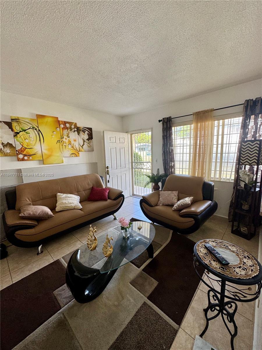 A living room features a brown sofa, matching armchair, glass coffee table, and tiled floors — 71 NW 76th St # 5, Miami FL 33150, MIAMI, FL