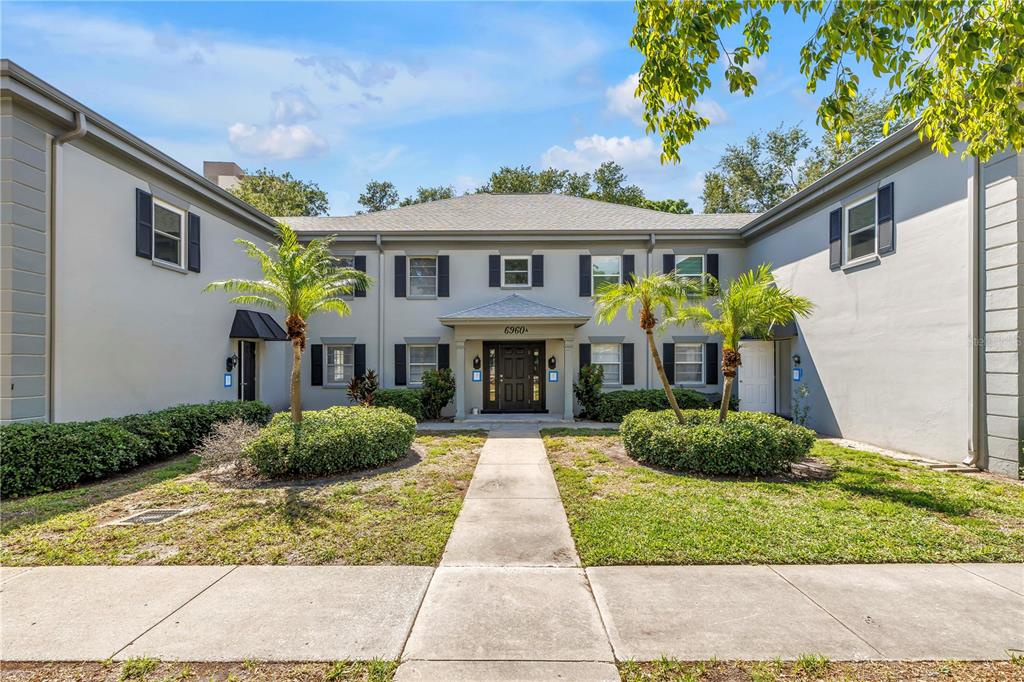 A two-story apartment building features a central entrance, gray stucco siding, and landscaped front yards — 6960 SUNSET DRIVE S UNIT 1A, SOUTH PASADENA, FL