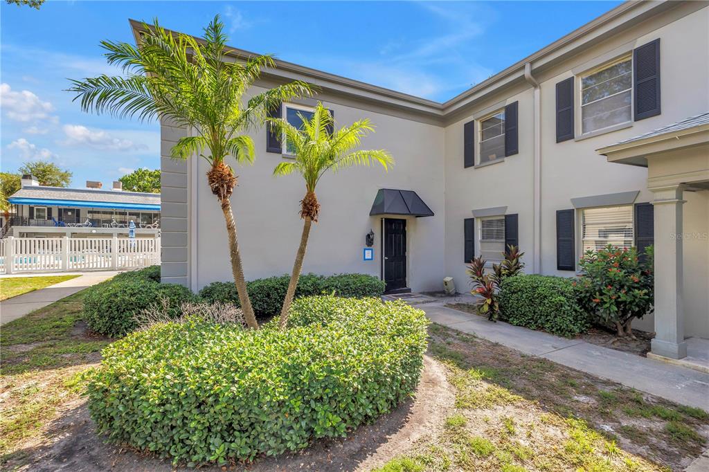 A two-story townhouse exterior features a black front door, two palm trees, and manicured hedges — 6960 SUNSET DRIVE S UNIT 1A, SOUTH PASADENA, FL