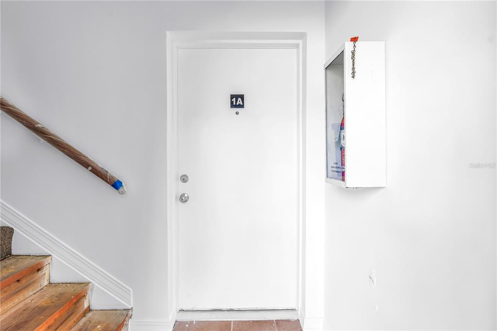 A white door labeled 1A is positioned next to a staircase and a wall-mounted cabinet — 6960 SUNSET DRIVE S UNIT 1A, SOUTH PASADENA, FL