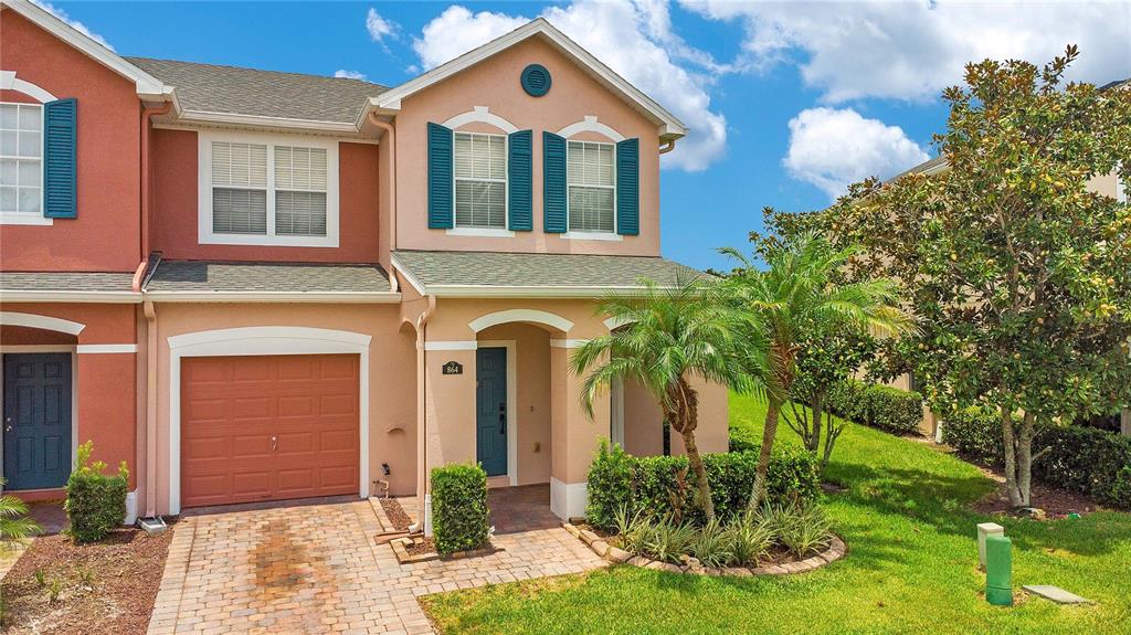 A two-story townhouse with a tan stucco exterior, teal shutters, and a brick paver driveway — 864 PARK GROVE COURT, ORLANDO, FL
