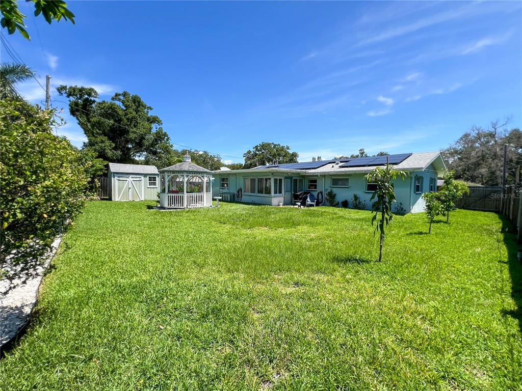 A backyard features a light green house with solar panels, a white gazebo, and a shed — 1524 S FREDRICA AVENUE, CLEARWATER, FL