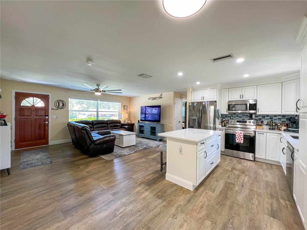 An open-concept living room and kitchen featuring white cabinetry, a center island, and wood flooring — 1524 S FREDRICA AVENUE, CLEARWATER, FL