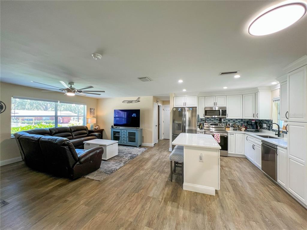 An open-concept living room and kitchen with white cabinets, stainless appliances, and wood-look flooring — 1524 S FREDRICA AVENUE, CLEARWATER, FL