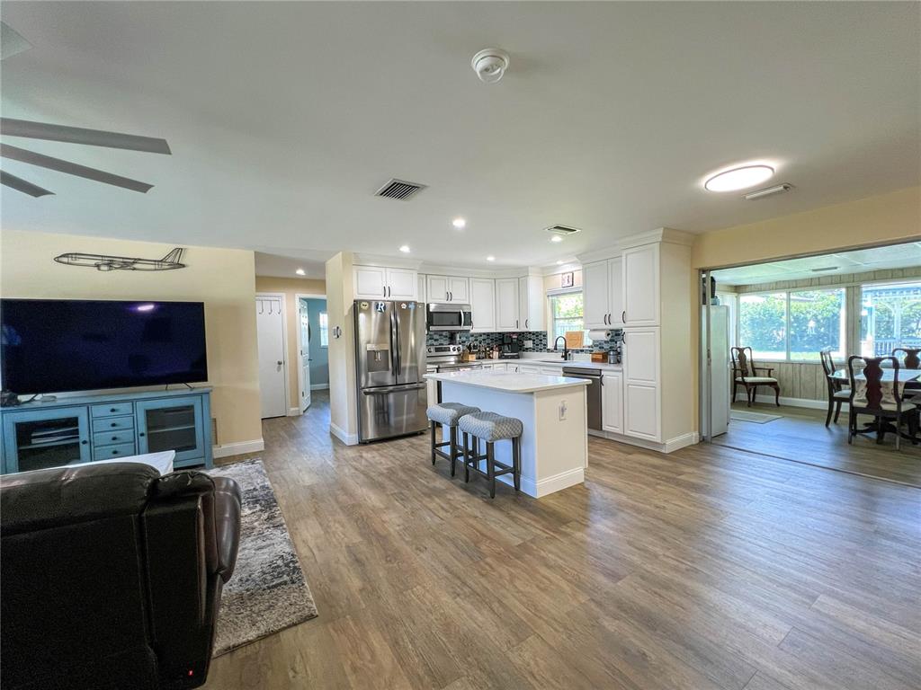 An open-concept kitchen and living area features white cabinetry, a center island, and wood-look flooring — 1524 S FREDRICA AVENUE, CLEARWATER, FL