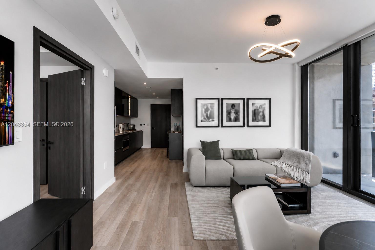 A modern living room features a grey sectional sofa, black accents, and a contemporary light fixture — 20 NE 11th Street # 3410, Miami FL 33132, MIAMI, FL